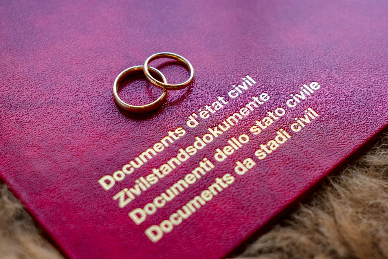 Zwei goldene Eheringe liegen auf der roten Mappe mit der Aufschrift Zivilstandsdokumente