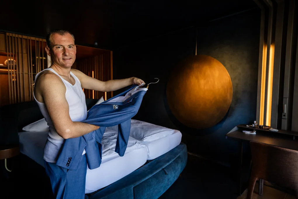 Bräutigam zieht im Hotelzimmer sein Hemd an, gedämpftes Licht