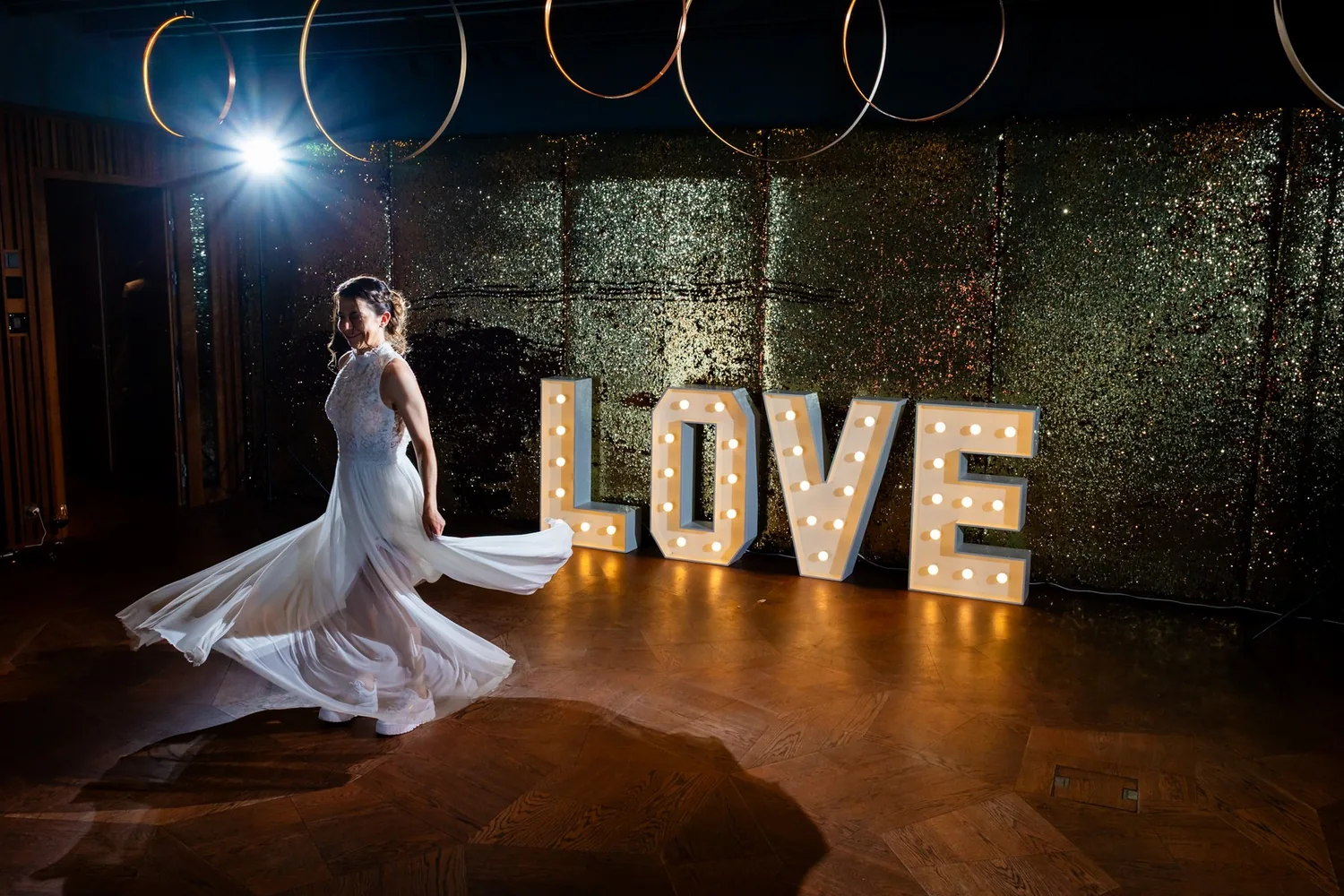 Braut dreht sich vor beleuchteten LOVE-Buchstaben, das Kleid schwingt mit