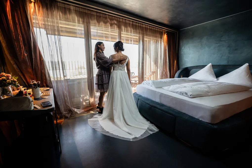 Braut wird im Hotelzimmer am Fenster fertig gemacht, natürliches Licht von der Seite