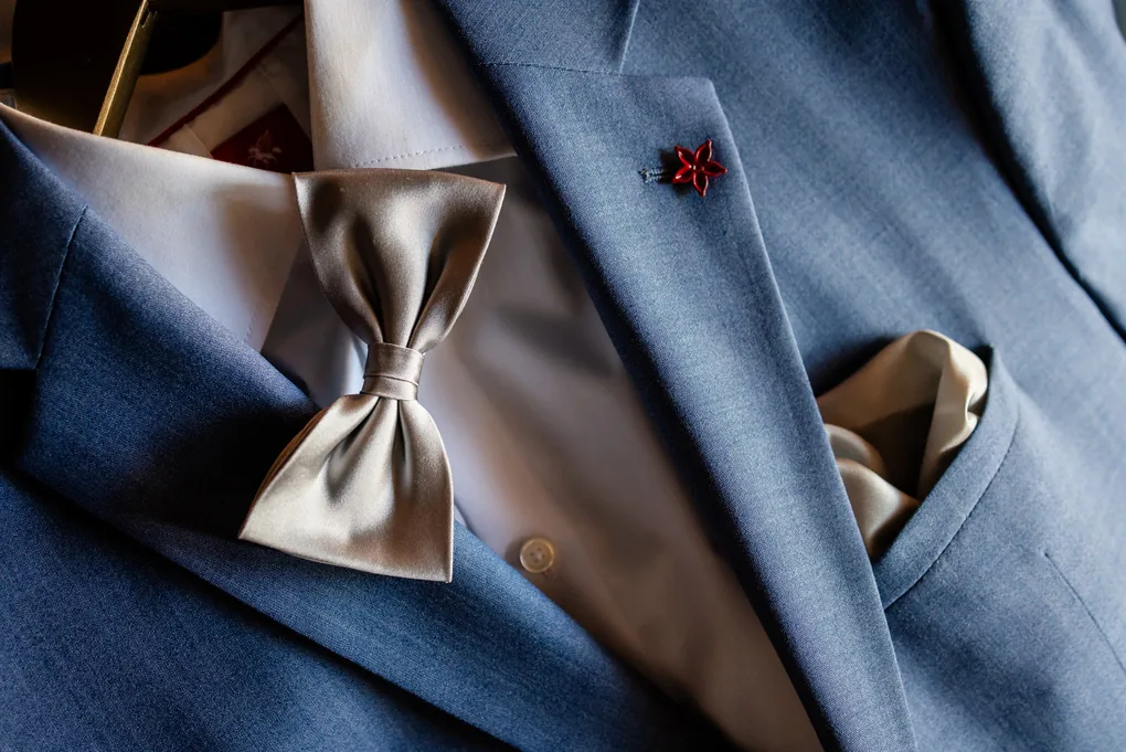 Detailaufnahme einer Fliege und eines Anstecksträusschens auf blauem Anzugstoff