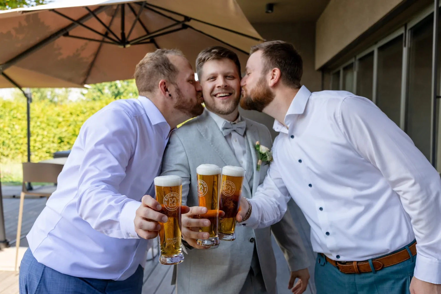 Drei Männer stossen unter einem Sonnenschirm auf der Terrasse mit Bier an