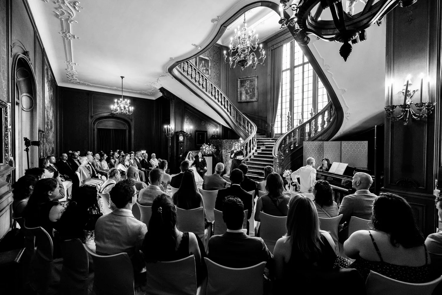Schwarzweissaufnahme der Trauung in der Halle mit den Gästen in Reihen