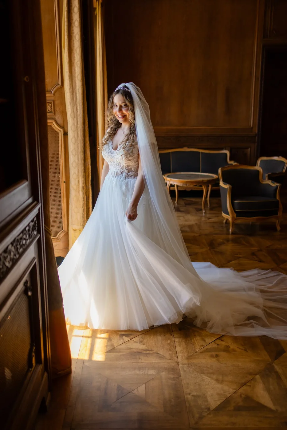 Braut steht im Licht einer hohen Fenstertür in einem Salon der Villa