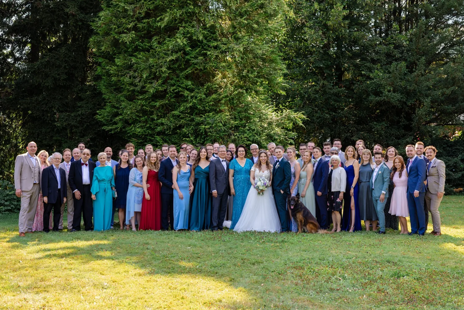 Die ganze Hochzeitsgesellschaft auf der Wiese im Park vor hohen Bäumen