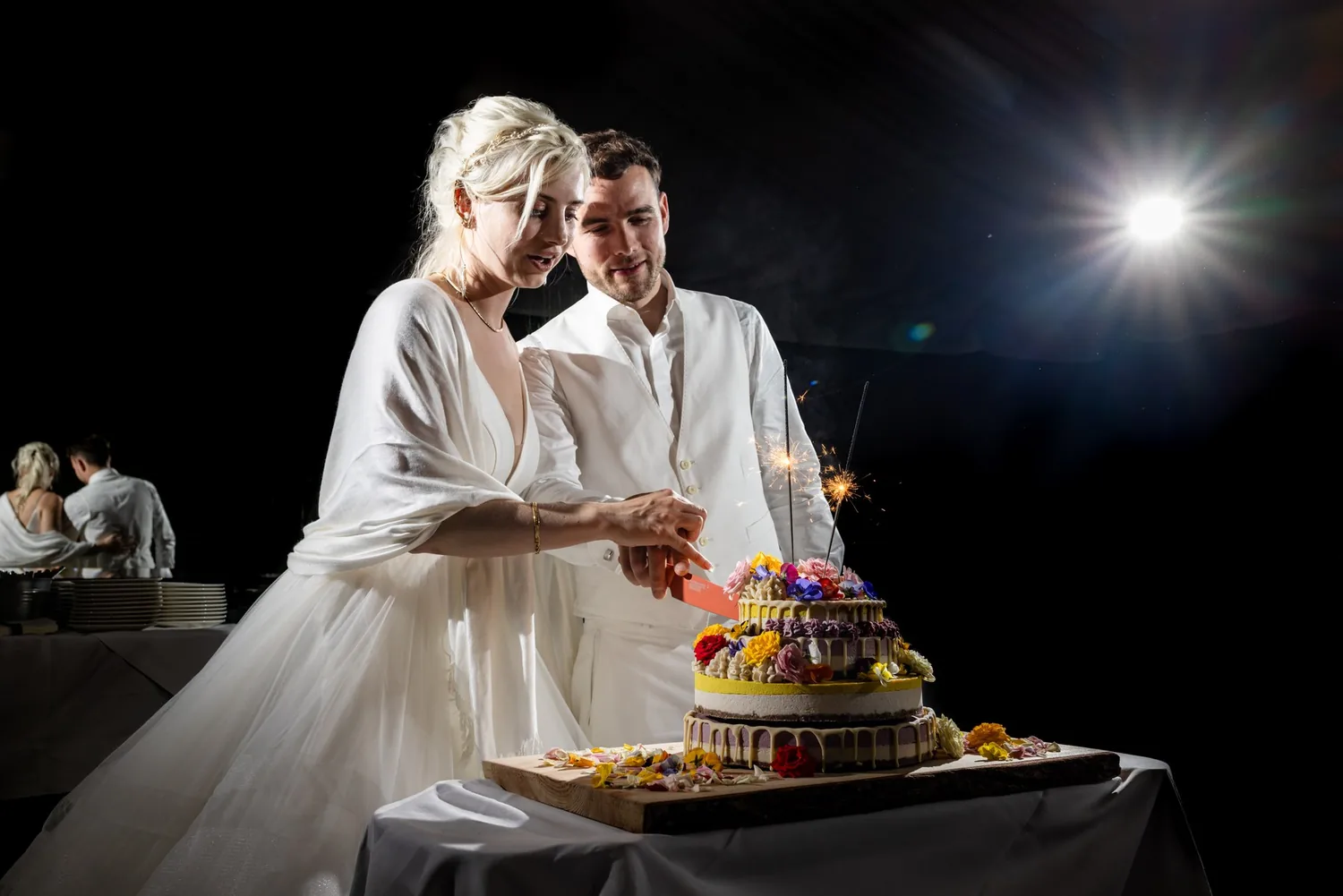 Brautpaar schneidet am Abend die Hochzeitstorte an, angeblitzt vor dunklem Hintergrund