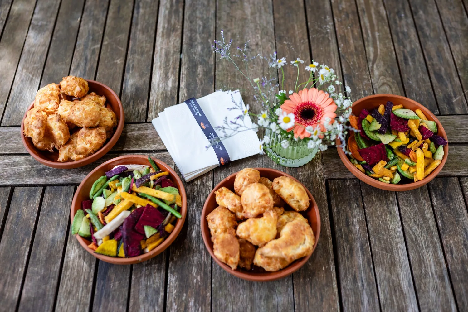 Schalen mit Apéro-Häppchen und Blumen auf einem verwitterten Holztisch