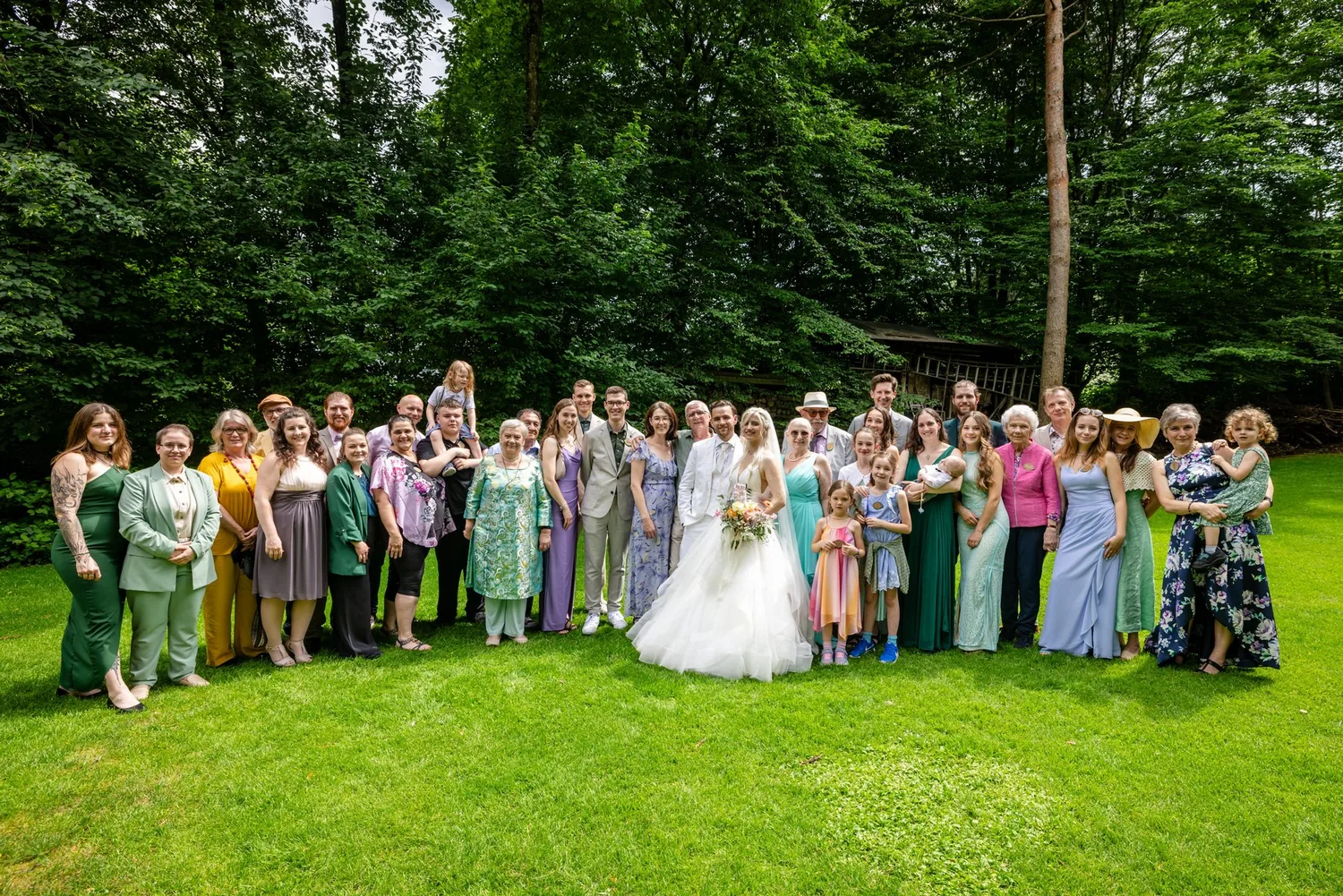 Grosses Gruppenfoto der Hochzeitsgesellschaft auf der Wiese vor dem Wald