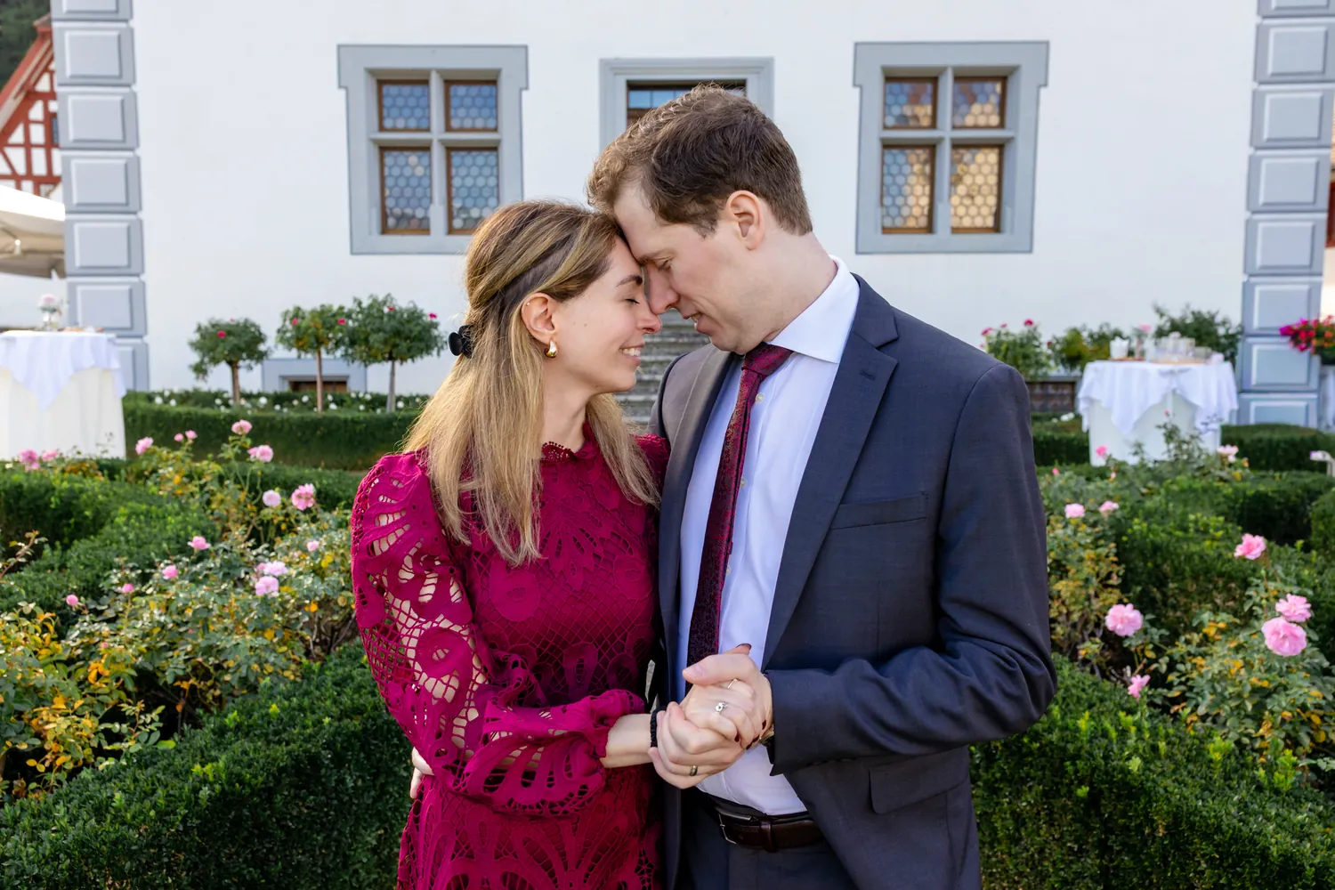Braut im Spitzenkleid in Merlot mit dem Bräutigam im Rosengarten