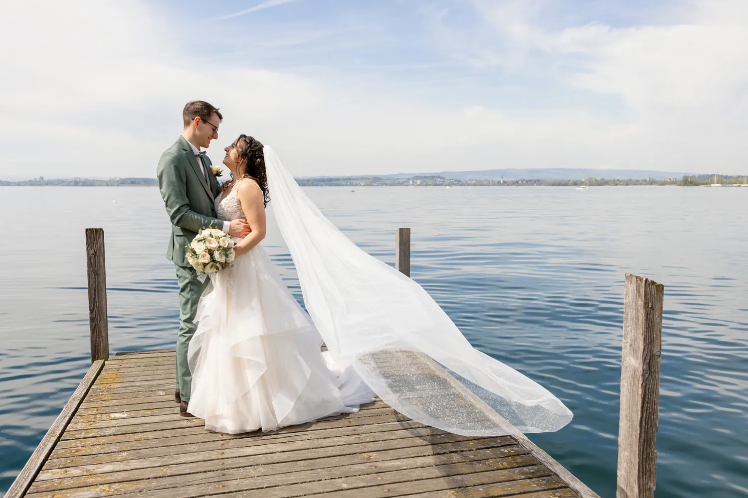 Brautpaar auf einem Holzsteg am Zugersee, der lange Schleier weht im Wind
