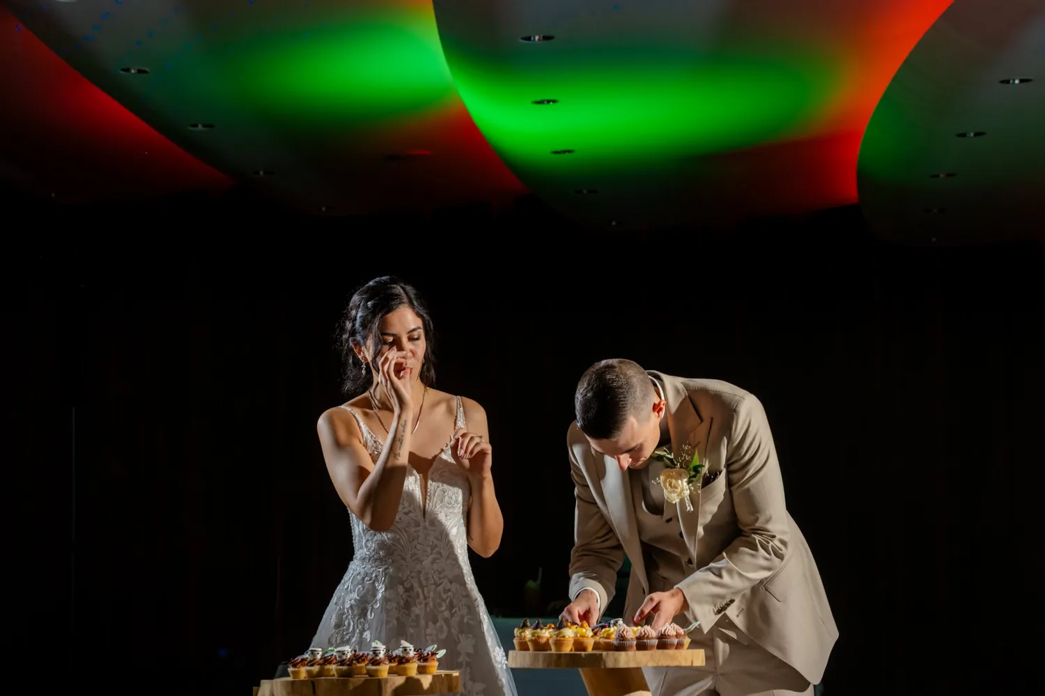 Das Brautpaar nascht am Abend von den Cupcakes, über ihnen farbiges Licht