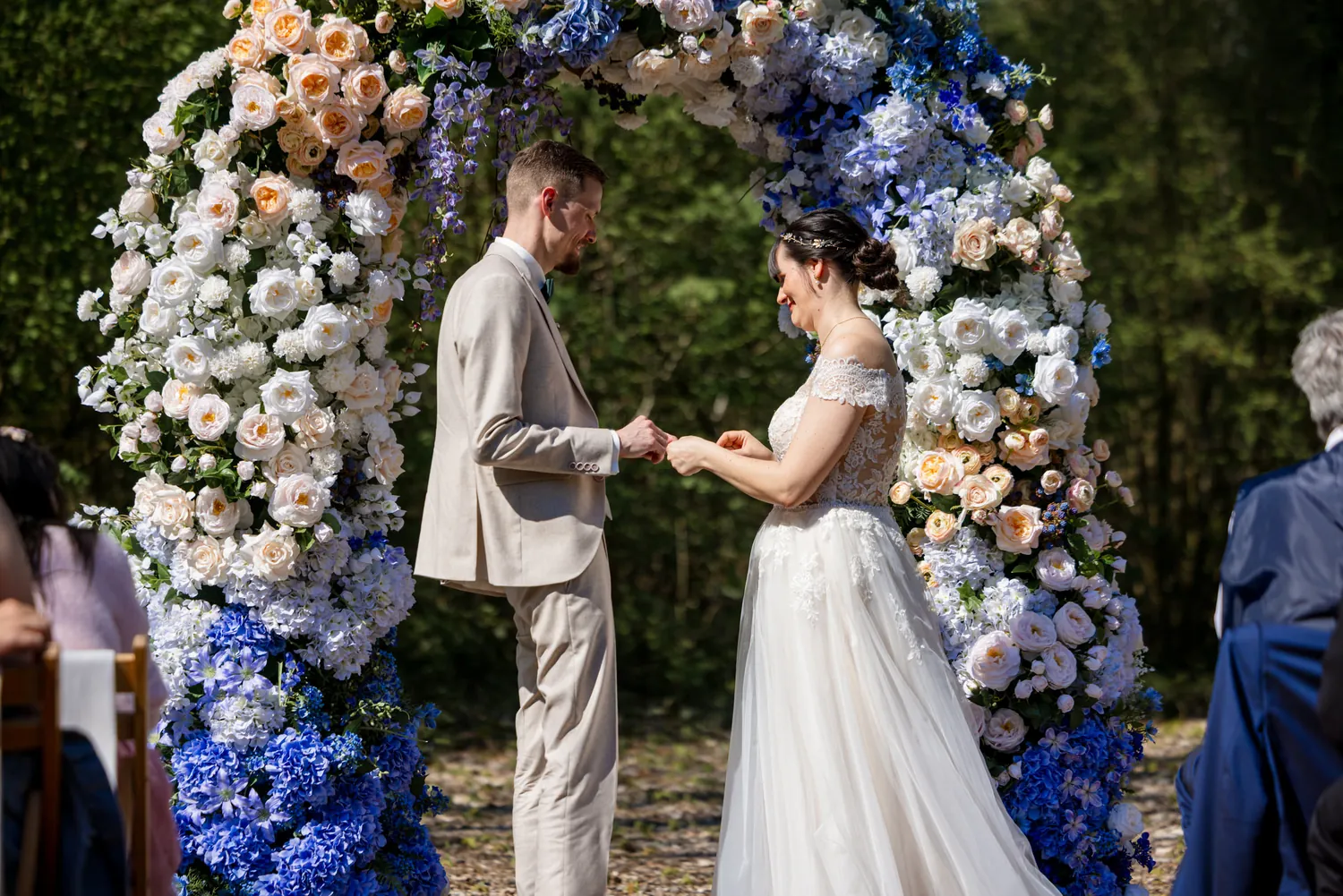 Ringtausch bei der freien Trauung unter einem Bogen aus Rosen und blauen Hortensien