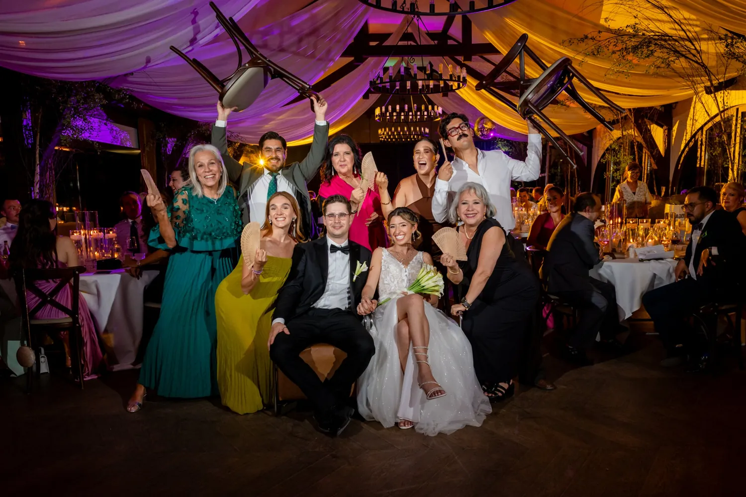 Speed-Gruppenfoto am Abend im Festsaal: das Paar sitzt, die Gäste heben Stühle und Fächer