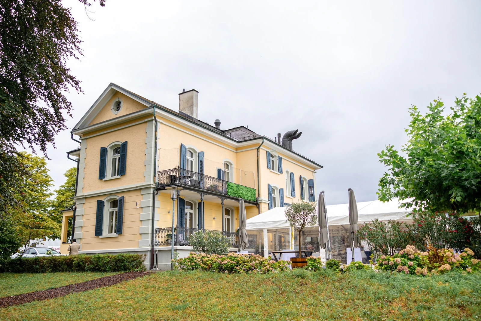 Die Villa am See in Goldach von aussen, gelbe Fassade mit blaugrauen Läden, daneben der Pavillon