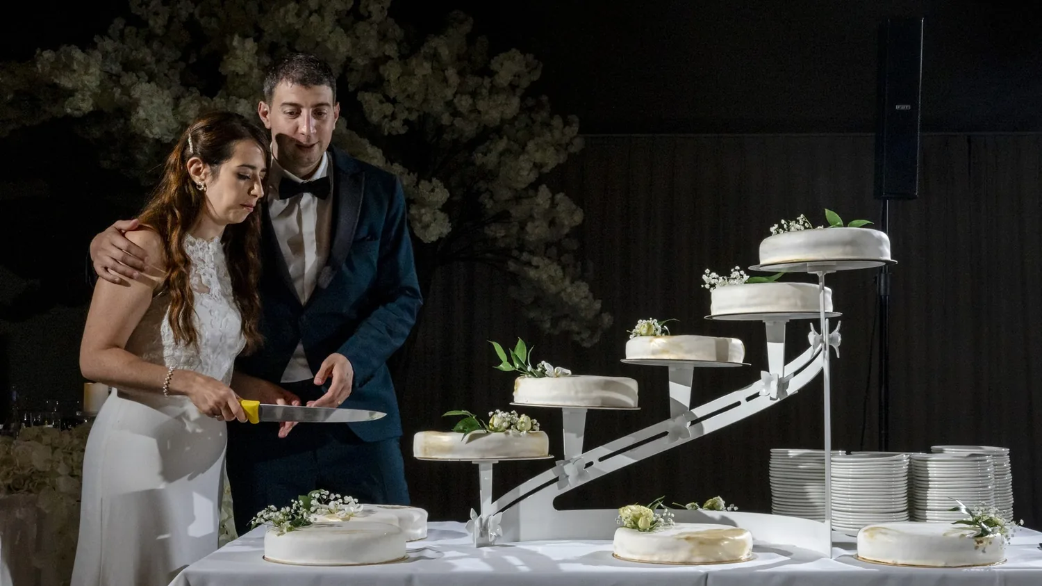 Brautpaar schneidet am Abend die Hochzeitstorte an, angeblitzt vor dunklem Hintergrund