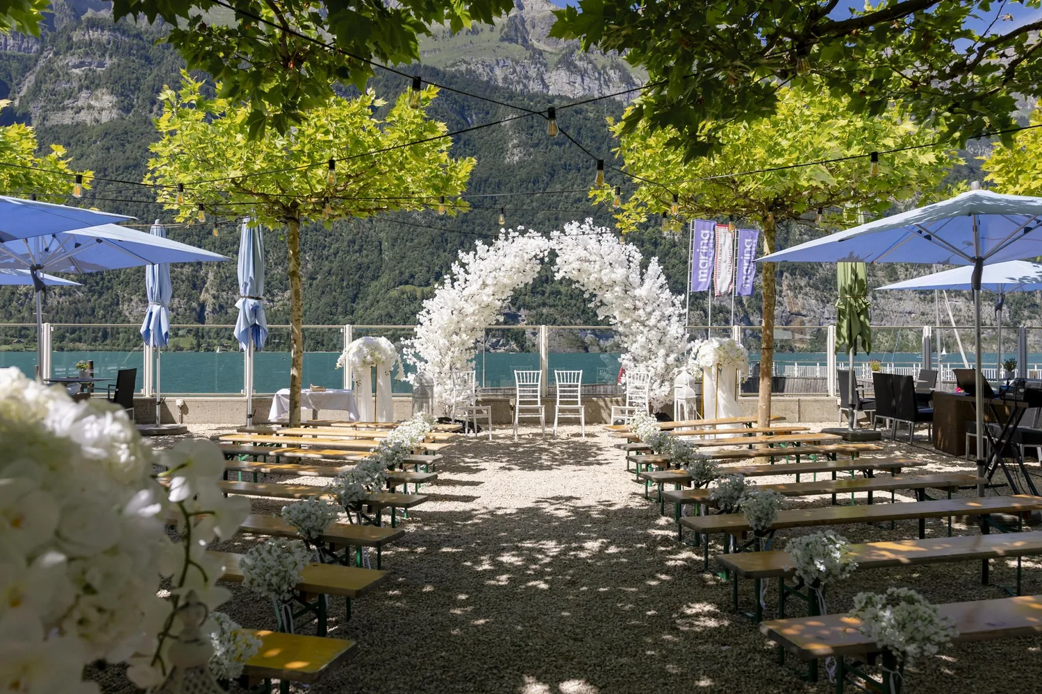 Weisser Blumenbogen im Hafengarten der Marina Walensee, dahinter der See und die Berge