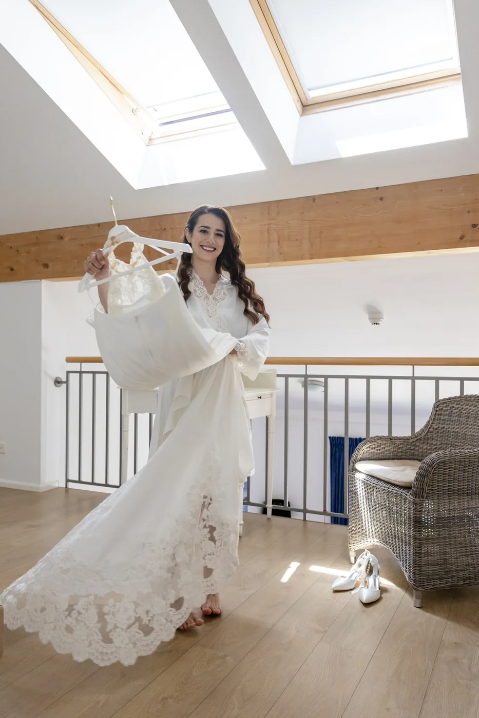 Braut hält ihr Hochzeitskleid im Zimmer unter dem Dachfenster