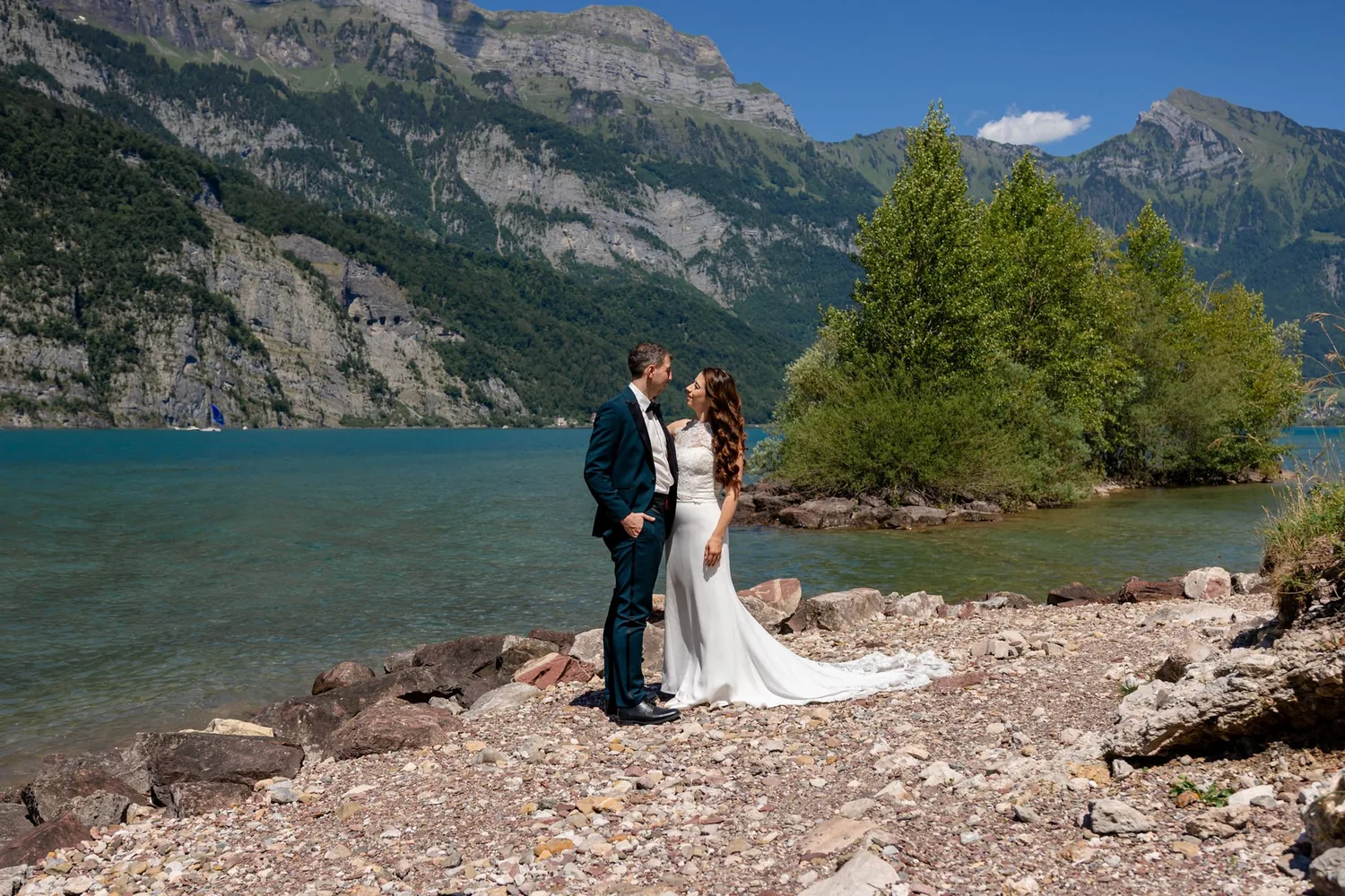 Brautpaar steht am steinigen Ufer des Walensees, dahinter das gegenüberliegende Bergufer