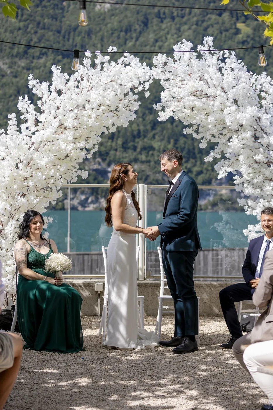 Brautpaar steht bei der freien Trauung vor dem weissen Blumenbogen, dahinter der Walensee