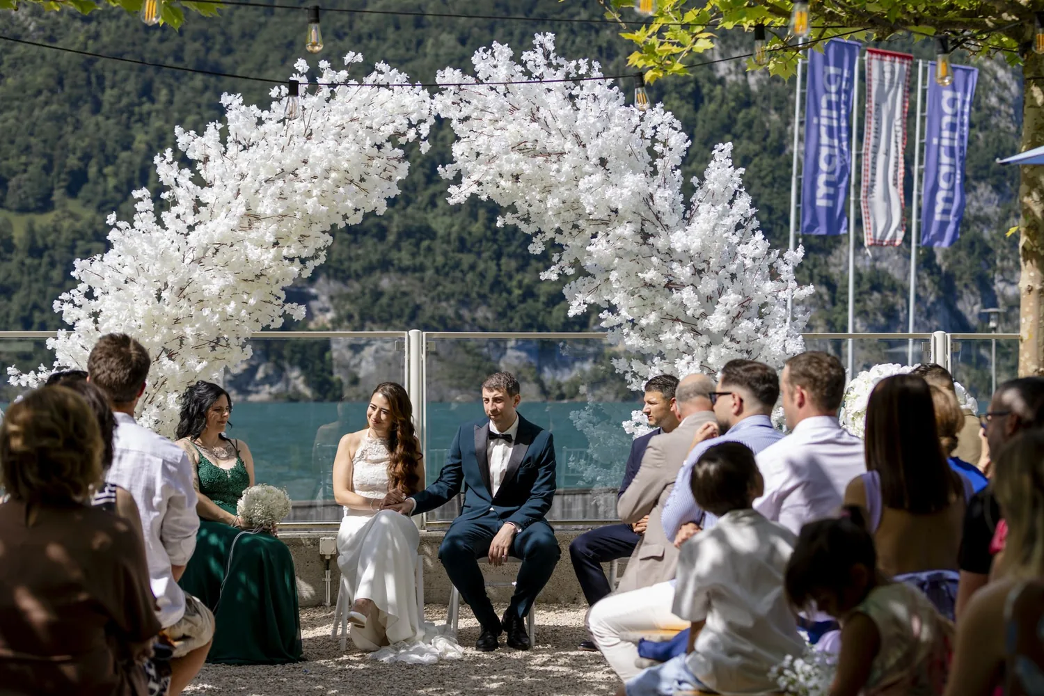 Freie Trauung unter dem weissen Blumenbogen im Hafengarten, die Gäste sitzen mit Blick auf den Walensee