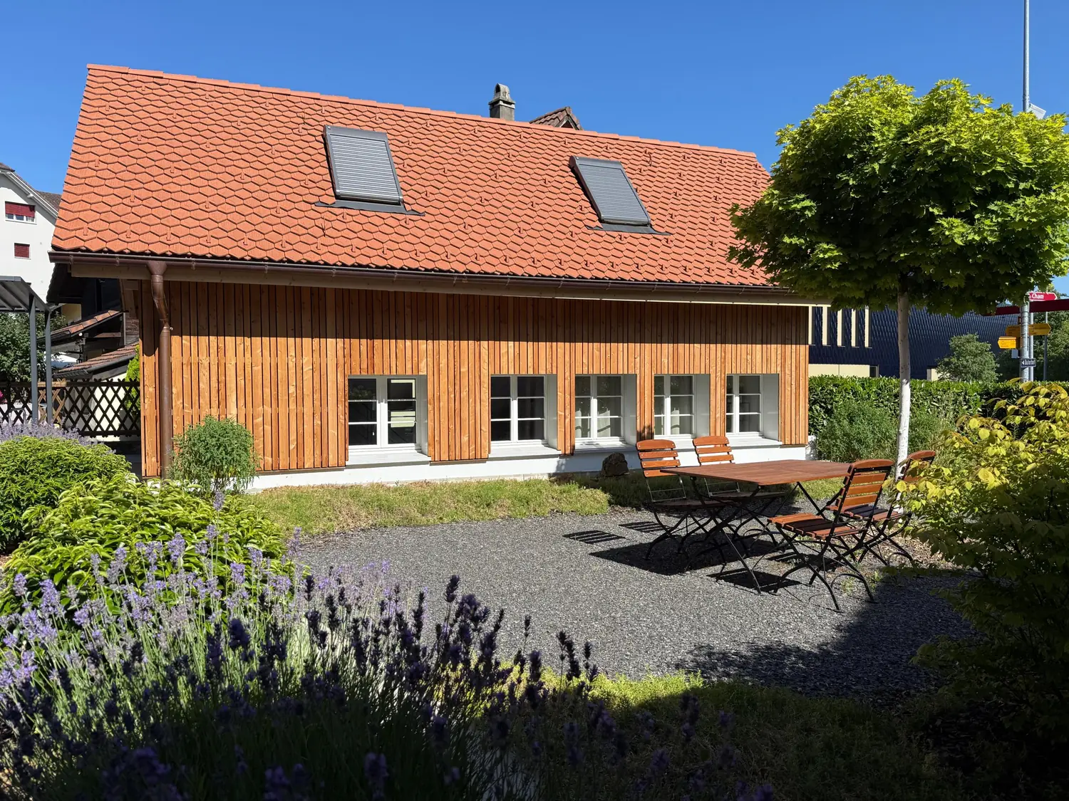 Das Holzhaus des Studios von der Gartenseite, mit Sitzplatz, Lavendel und Ahornbaum