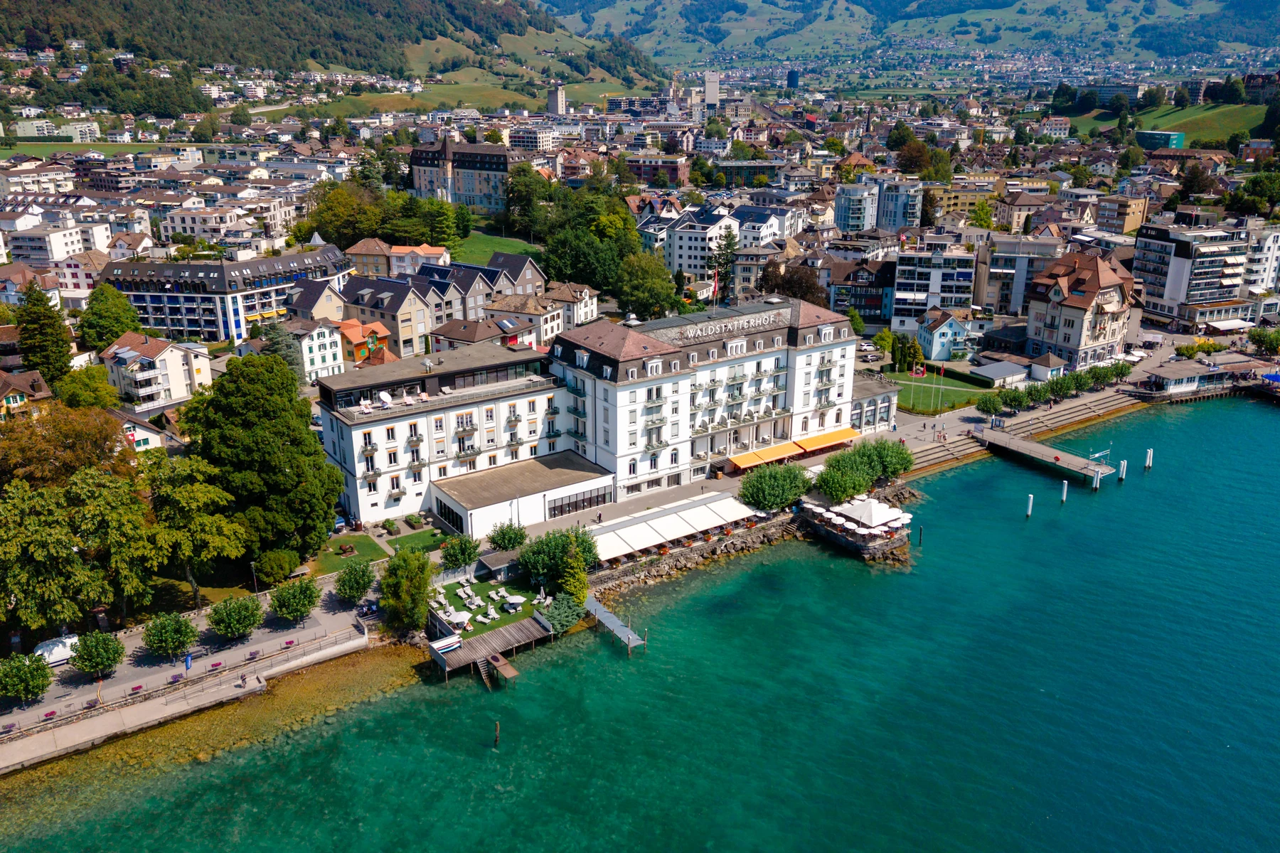 Luftaufnahme des Seehotels Waldstätterhof in Brunnen, davor der Vierwaldstättersee mit Steg und Liegewiese